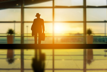 Silhouettes of alone businessman with luggage blurred sunset background at airport terminal