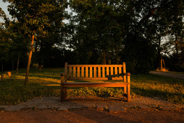 A lone wooden bench on a path through the forest to Spilberk Castle Brno Czech Republic during a summer evening at sunset with rays shining on the bench in orange color tone.