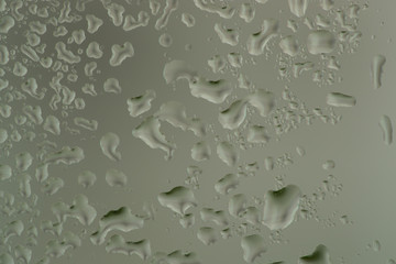 Closeup macro photo of water drops captured on glass window with dark background overlooking city street.