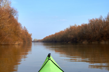 Autumn kayaking on a green kayak along the nature reserve in the Danube river. Autumn brown trees on the banks of Danube river on a clear autumn day.