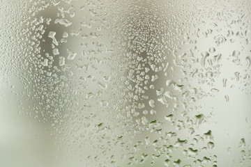 Closeup macro photo of water drops captured on glass window with dark background overlooking city street.
