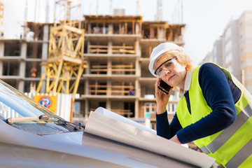 Builder woman at construction site in a green vest and a white helmet with the tablet. Middle-aged woman with glasses studying the project.