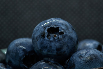 Macro closeup photo of blueberries laying on top of each other in a plate washed with fresh water and with reflection of ambient light.