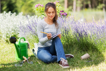 gardening and people concept - young woman writing to notebook at summer garden