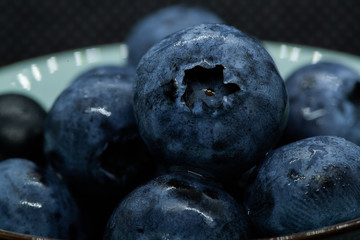 Macro closeup photo of blueberries laying on top of each other in a plate washed with fresh water and with reflection of ambient light.