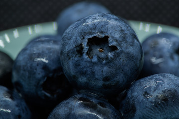 Macro closeup photo of blueberries laying on top of each other in a plate washed with fresh water and with reflection of ambient light.