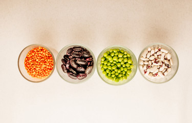 Collection set of various dried legumes in glass cups arranged horizontally green peas, red lentils, red beans, white beans close-up on a white background