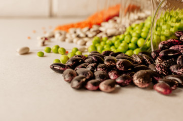 A set of different dried legumes is in glass cups and is a little scattered: red lentils, green peas, red beans, white beans. Selective Focus on Red Beans