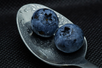 Blueberries Macro close-up photo of stacked and side by side in a teaspoon on a dark background covered with small drops of water.
