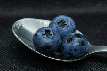 Blueberries Macro close-up photo of stacked and side by side in a teaspoon on a dark background covered with small drops of water.