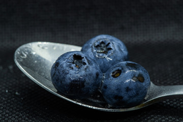 Blueberries Macro closeup photo of superimposed on top of each other and tiled in a teaspoon on a dark background glistening in drops of fresh water.