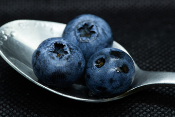 Blueberries Macro closeup photo of superimposed on top of each other and tiled in a teaspoon on a dark background glistening in drops of fresh water.