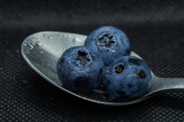 Blueberries Macro close-up photo of stacked and side by side in a teaspoon on a dark background covered with small drops of water.