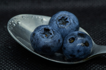 Blueberries Macro closeup photo of superimposed on top of each other and tiled in a teaspoon on a dark background glistening in drops of fresh water.