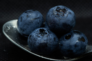 Blueberries Macro close-up photo of stacked and side by side in a teaspoon on a dark background covered with small drops of water.