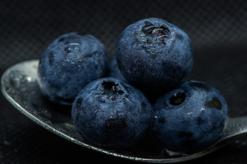 Blueberries Macro closeup photo of superimposed on top of each other and tiled in a teaspoon on a dark background glistening in drops of fresh water.