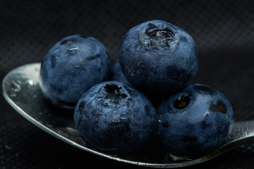 Blueberries Macro closeup photo of superimposed on top of each other and tiled in a teaspoon on a dark background glistening in drops of fresh water.