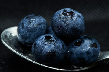 Blueberries Macro closeup photo of superimposed on top of each other and tiled in a teaspoon on a dark background glistening in drops of fresh water.