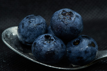 Blueberries Macro closeup photo of superimposed on top of each other and tiled in a teaspoon on a dark background glistening in drops of fresh water.