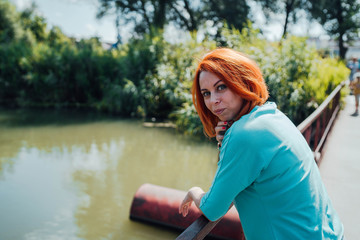 Portrait of an adult red-haired woman in casual clothes is standing on the bridge