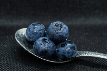 Blueberries Macro close-up photo of stacked and side by side in a teaspoon on a dark background covered with small drops of water.