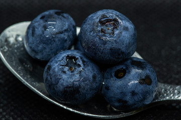 Blueberries Macro close-up photo of stacked and side by side in a teaspoon on a dark background covered with small drops of water.