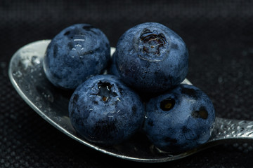 Blueberries Macro close-up photo of stacked and side by side in a teaspoon on a dark background covered with small drops of water.