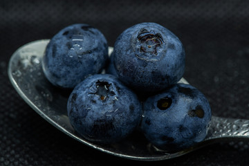 Blueberries Macro close-up photo of stacked and side by side in a teaspoon on a dark background covered with small drops of water.
