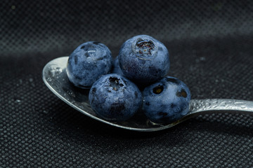 Blueberries Macro close-up photo of stacked and side by side in a teaspoon on a dark background covered with small drops of water.