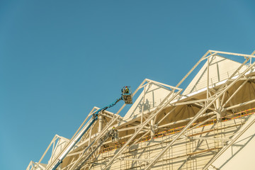 Painter, plasterer in special clothes, paint the facade of the building with white paint roller at...