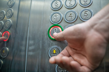 The thumb presses the button in the elevator zero floor close-up. The elevator buttons are signed...