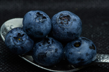 Blueberries Macro closeup photo of superimposed on top of each other and tiled in a teaspoon on a dark background glistening in drops of fresh water.