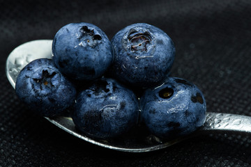 Blueberries Macro closeup photo of superimposed on top of each other and tiled in a teaspoon on a dark background glistening in drops of fresh water.