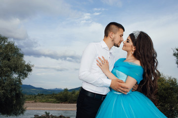 Pretty young romantic couple spend time together. Beautiful brunette girl with a perfectly curly hair. A loving couple kissing near river. Love story of the beautiful young man and woman.