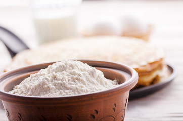 Stack of French crepes in frying pan on wooden kitchen table with milk eggs and flour aside