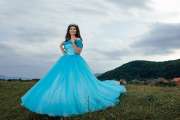 Beautiful unusual woman walking and posing in blue dress. Beauty romantic girl outdoors enjoying nature. Portrait of romantic female. Beautiful, elegant, hairstyle with jewelry. 