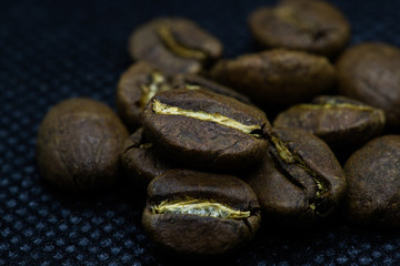 Closeup macro view of coffee beans laid on a black background after roasting in the apparatus.