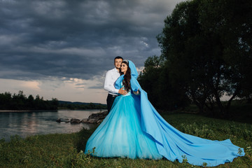 Fototapeta premium The guy and the girl on nature at sunset. A pair of lovers embrace against the backdrop of a beautiful river landscape. Tourism in the wild nature. Dawn in the mountains in summer