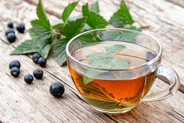 Herbal tea from currant leaves in a glass transparent cup on a wooden table near the green leaves and currant berries.