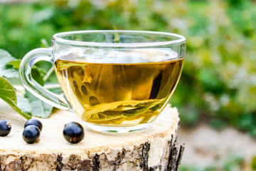A cup of tea with black currant leaves. Tea with currants on a wooden table in the open air.
