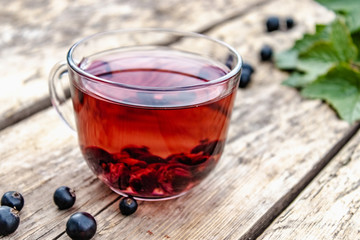 A cup of tea with black currants on a wooden table next to green leaves and currant berries.