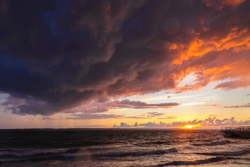Dramatic sunset through a cloudy dark sky over the ocean.