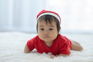 Cute Sweet Adorable Asian Baby wearing Santa hat and cloth costume lying on white carpet smiling and playing with happiness emotional in cozy bedroom,Healthy Baby Concept