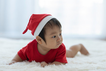 Cute Sweet Adorable Asian Baby wearing Santa hat and cloth costume lying on white carpet smiling and playing with happiness emotional in cozy bedroom,Healthy Baby Concept