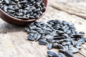 A pile of sunflower seeds in a bowl on a wooden background. Sunflower seeds scattered on the table.