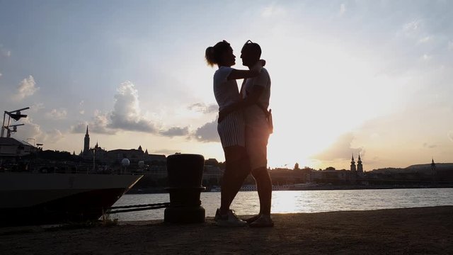 silhouette of romantic couple hugging and kissing on pier at sunset