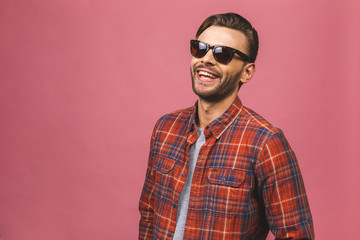 Portrait of a handsome happy cool young man in sunglasses enjoying over pink background.