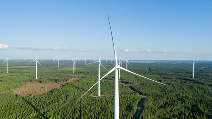 Fototapeta na wymiar Wind turbine near green forest, beautiful aerial landscape with blue sky. Producing energy in environmentally friendly way. close up.