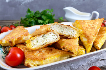 Tasty fried puff patties from thin Armenian lavash on a wooden table. Envelopes from pita bread cottage cheese filling.