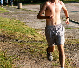 Shirtless runner training in the heat on grass at a park
